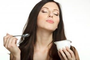 Young female enjoying taste of yogurt isolated on white