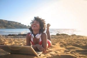 Girl using her laptop in a paradise beach, she is laughing and listening music with her headphones.