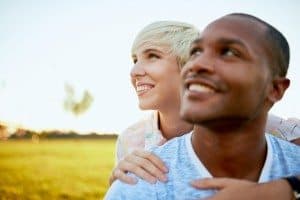 Diverse couple in love hanging out in a city parc with girlfriends wrapping her arms around boyfriend for public display of affection