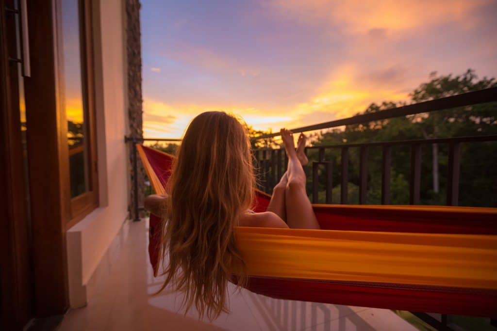 Young woman enjoys sunset relaxing in the hammock on the balcony