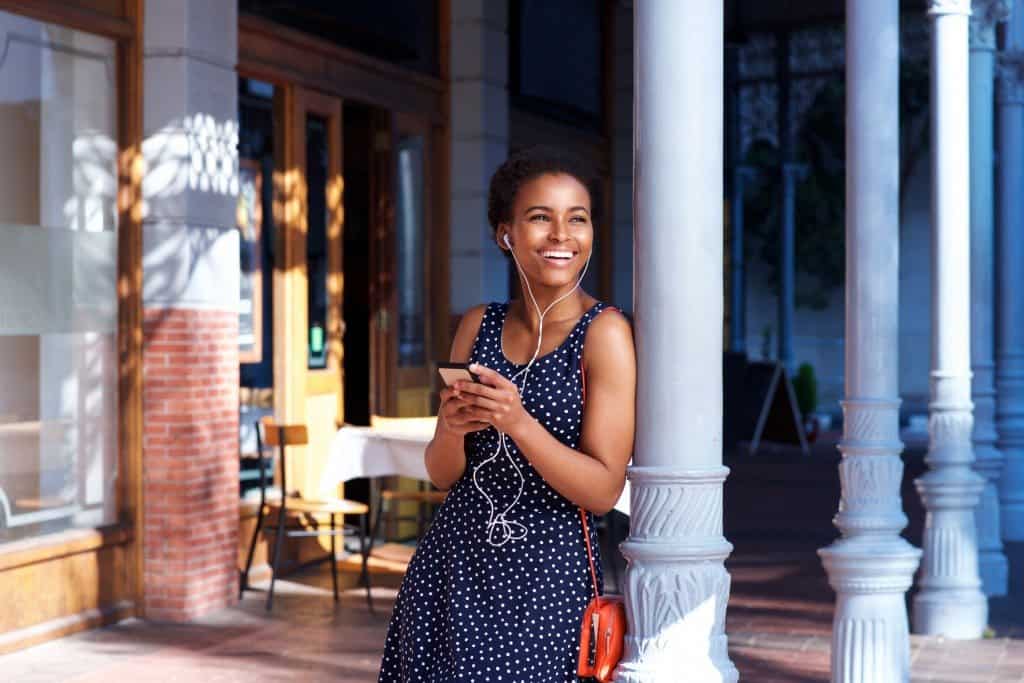 Portrait of smiling young woman standing outside with earphones and mobile phone