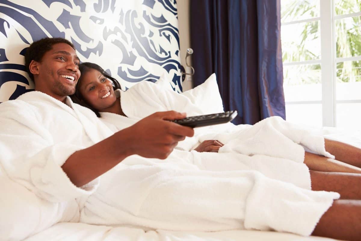 Couple Relaxing In Hotel Room Watching Television Lying On Bed Smiling